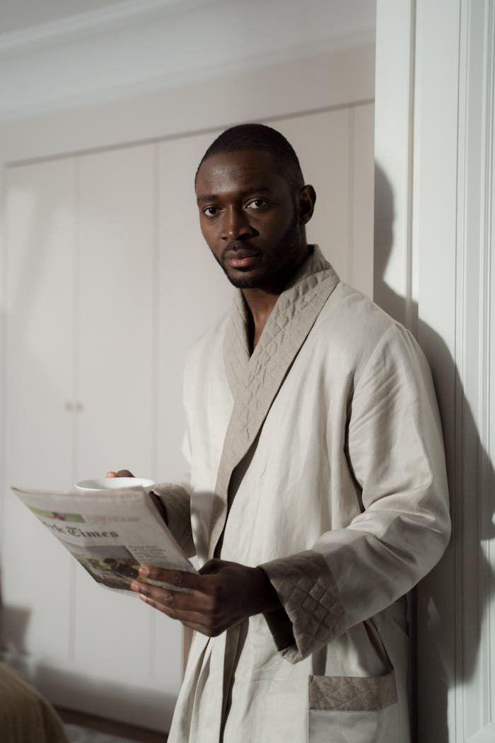 Adult man in bathrobe holding a newspaper indoors, relaxing morning scene.