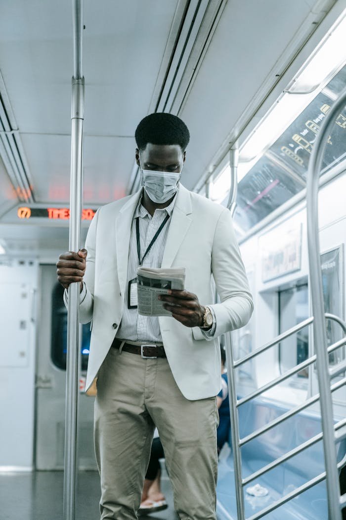 An adult man wearing a mask reads a newspaper on a subway train, reflecting pandemic life.